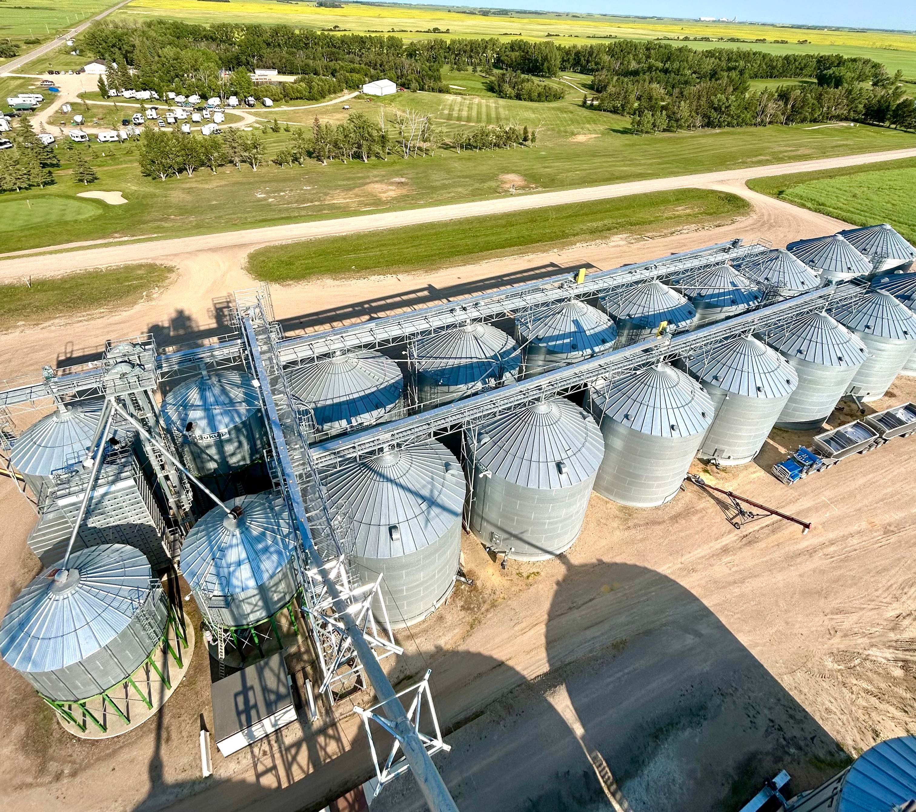Looking down from the top of a tower at galvanized catwalks and conveyors running over two rows of grain bins