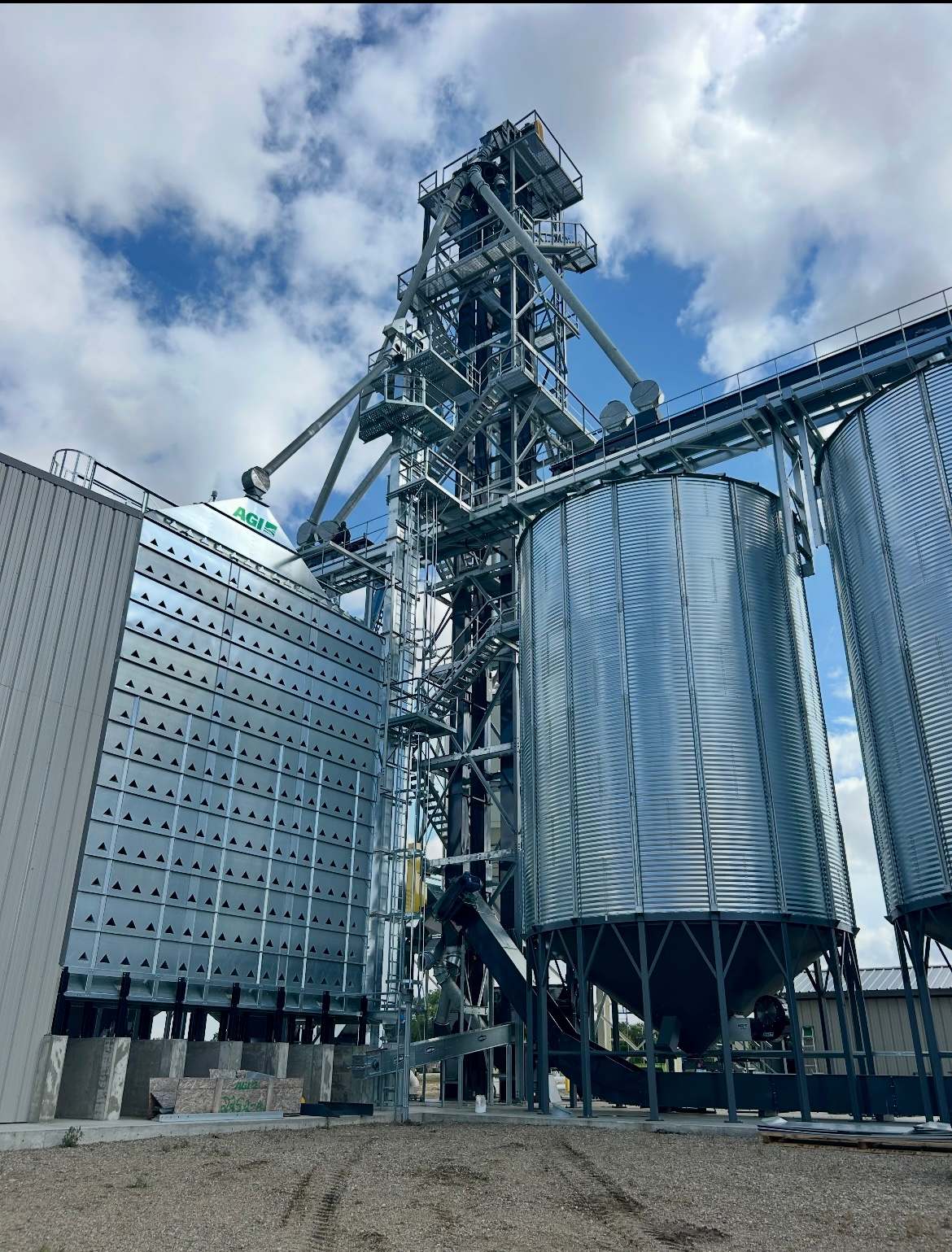 Galvanized stair tower and elevator leg rising between a grain dryer and hopper bins